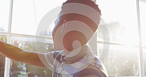 African american boy opening curtain and looking out of sunny window, backlit by sun