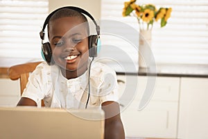 African American boy playing game on digital tablet at dining table in kitchen