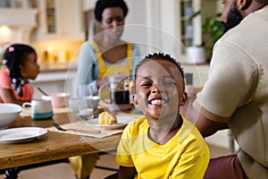 African american boy smiling and looking at camera while having breakfast with family at table