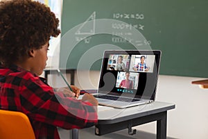 African american boy using laptop for video call, with diverse smiling high school pupils on screen