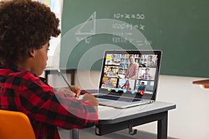 African american boy using laptop for video call, with diverse smiling high school pupils on screen