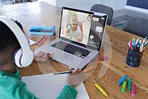 African american boy using laptop for video call, with smiling elementary school pupil on screen