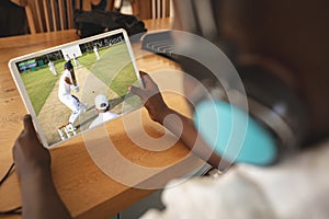 African american boy wearing headphones at home watching baseball game on tablet