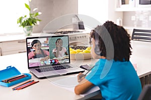 African american boy wearing headphones looking at laptop screen with girls during online lecture