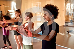 African american boy working out using resistance band together with other kids in gym. Sport, healthy lifestyle