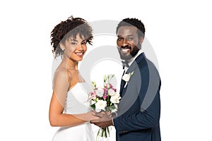 African american bride holding bouquet near bridegroom and looking at camera isolated on white