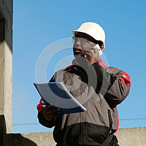 African american builder with work papers talks on smartphone