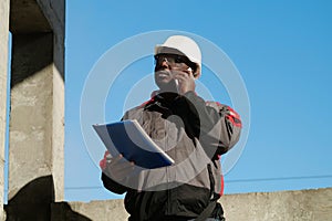 African american builder with work papers talks on smartphone