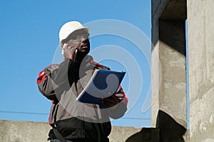 African american builder with work papers talks on smartphone