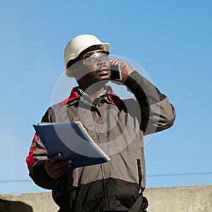 African american builder with work papers talks on smartphone