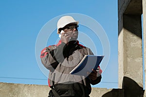 African american builder with work papers talks on smartphone