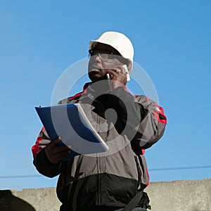 African american builder with work papers talks on smartphone