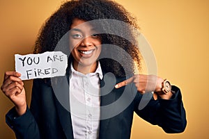 African american business boss woman with afro hair holding you are fired paper for dismissal with surprise face pointing finger