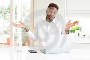 African american business man working using laptop clueless and confused expression with arms and hands raised