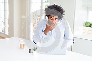 African American business man working using laptop cover mouth with hand shocked with shame for mistake, expression of fear,