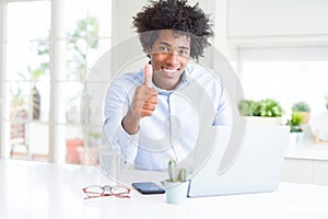 African American business man working using laptop happy with big smile doing ok sign, thumb up with fingers, excellent sign