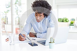 African American business man working writing on notebook scared in shock with a surprise face, afraid and excited with fear