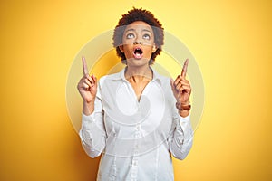 African american business woman over isolated yellow background amazed and surprised looking up and pointing with fingers and