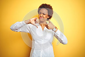 African american business woman over isolated yellow background Doing thumbs up and down, disagreement and agreement expression