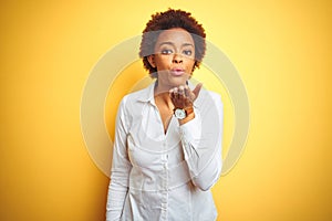 African american business woman over isolated yellow background looking at the camera blowing a kiss with hand on air being lovely