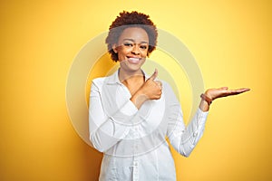 African american business woman over isolated yellow background Showing palm hand and doing ok gesture with thumbs up, smiling