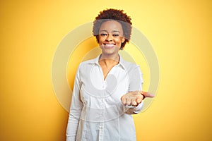 African american business woman over isolated yellow background smiling cheerful offering palm hand giving assistance and