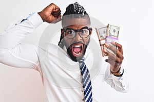 African american businessman with braids holding dollars over isolated white background annoyed and frustrated shouting with