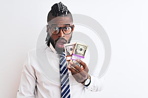African american businessman with braids holding dollars over isolated white background scared in shock with a surprise face,