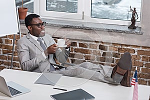 african american businessman with coffee cup putting feet up