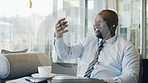 African American businessman in formal clothes laughing and talking to his family through smartphone video chat in airy