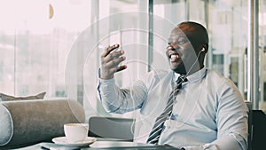 African American businessman in formal clothes laughing and talking to his family through smartphone video chat in airy