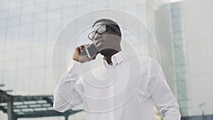 African American Businessman in glasses talking on cell phone, standing near his office