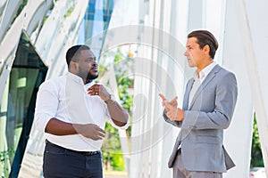 African-American businessman and his colleague in front of modern office building. Financial investors are talking