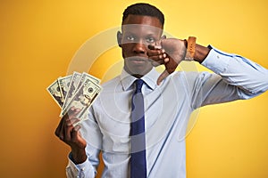 African american businessman holding dollars standing over isolated yellow background with angry face, negative sign showing
