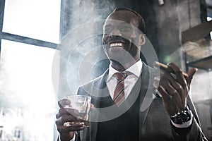 African american businessman holding glass with whiskey and smoking cigar