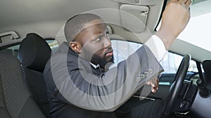 African-American businessman looking in car mirror to smarten beard and tie