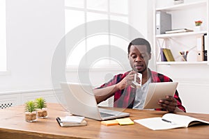 Black businessman in casual office, reading news on tablet, drinking coffee