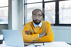 african american businessman sitting with crossed arms and looking at camera