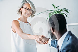 african american businessman and smiling caucasian businesswoman shaking hands