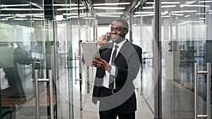 African american businessman talking on smartphone while walking in corporate office building and checking email