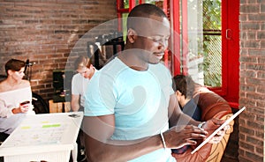 African American businessman is using a digital tablet and smiling while sitting in his office.