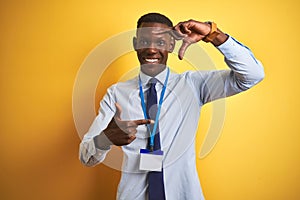 African american businessman wearing identification card over isolated yellow background smiling making frame with hands and