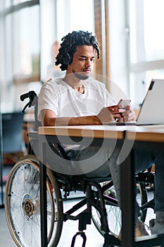 An African American businessman in a wheelchair takes a work break, using his smartphone while seated in a modern