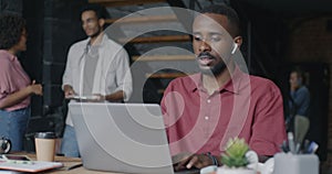African American businessman working with laptop and listening to music through earphones in loft style office