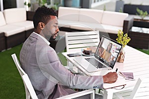 African american businessman writing in diary while video conferencing with colleague over laptop