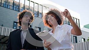 African American businesswoman with papers talking to Indian Arabian businessman client investor man pointing at urban