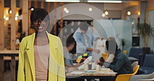 African-american businesswoman standing in the modern office, smiling and looking into the camera. Working people on the