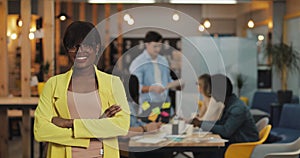 African-American businesswoman standing in the modern office, smiling and looking into the camera. Working people on the