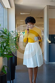 African american businesswoman talking on mobile phone holding mug at modern workplace