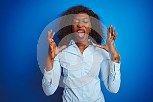 African american businesswoman wearing shirt standing over isolated blue background celebrating mad and crazy for success with